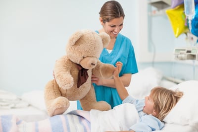 Nurse showing a teddy bear to a child in hospital ward