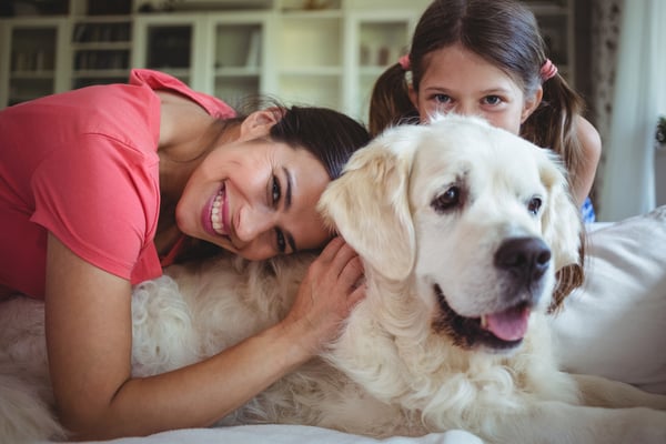 Mother and daughter sitting with pet dog in living room at home