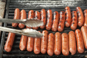 Picnic at a glance Pair of tongs reaching -- with motion blur -- toward shiny hot dogs on outdoor grill